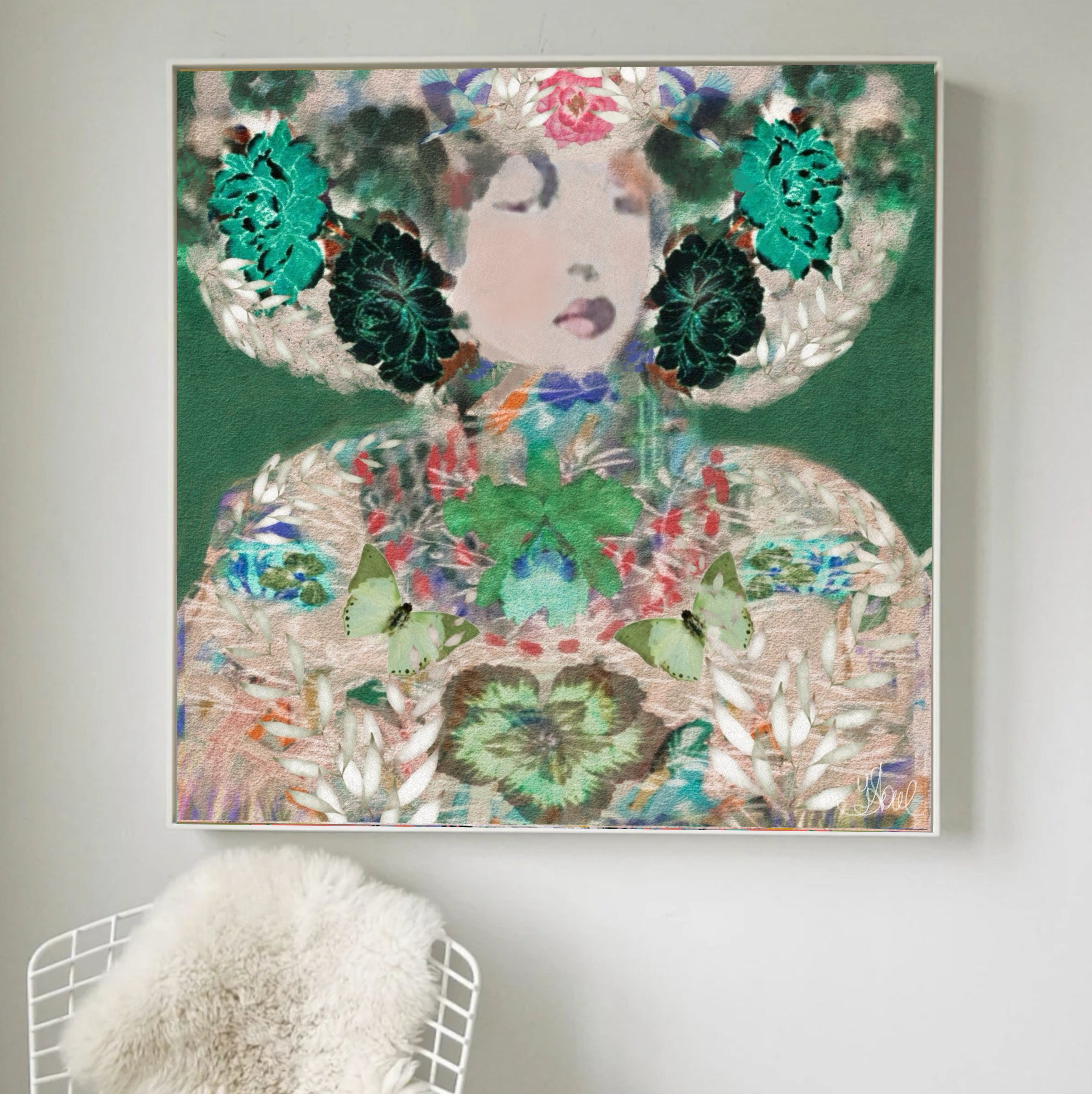 A square framed art print featuring a stylized woman's face and shoulders adorned with green leaves, flowers, and butterflies on a dark green background, displayed on a light gray wall above a white chair with a white faux-fur throw.