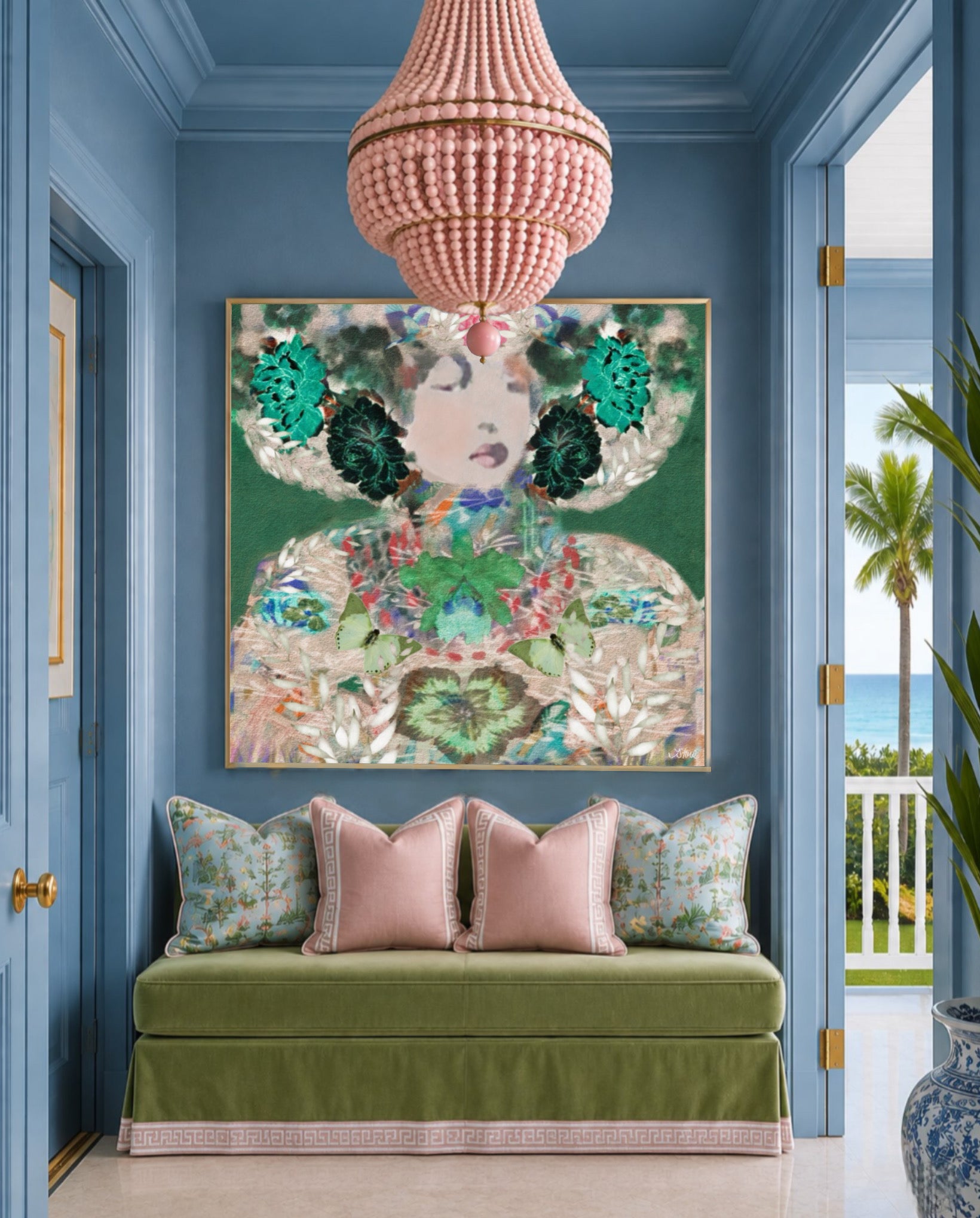 A large framed art print featuring a colorful, ornate portrait with green floral elements and gold detailing, displayed on a blue wall above a green velvet bench with pink pillows in a styled interior.