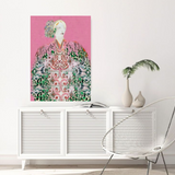 Framed artwork of  green and pink boho woman with floral hair on a pink background, displayed above a white cabinet in a room.