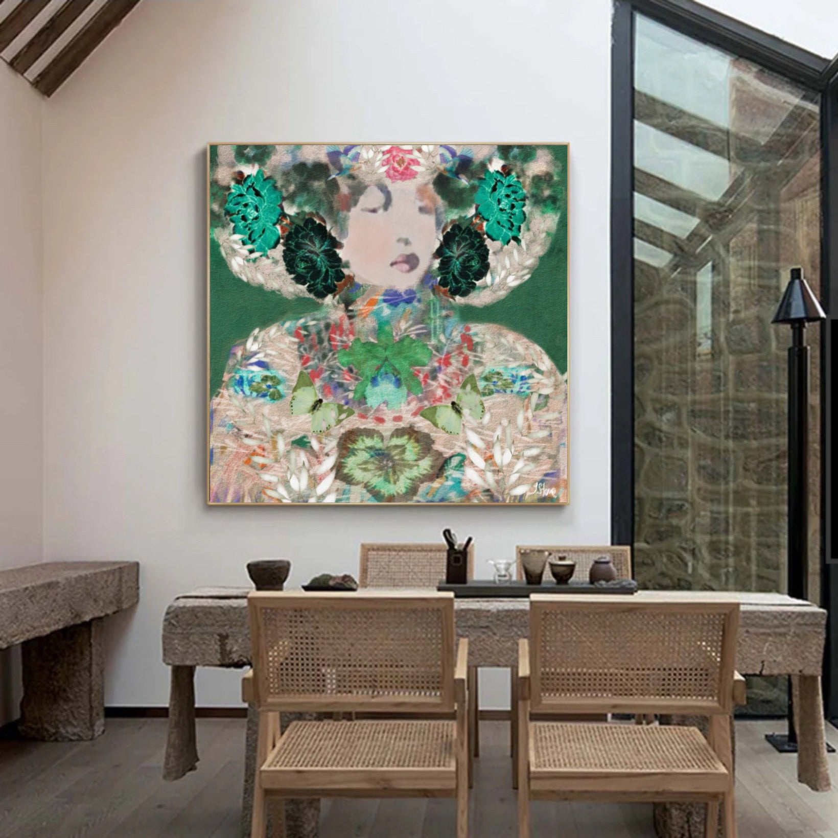 A colorful abstract painting of a woman with floral details hangs on a white wall in a modern dining room setting with a wooden table and woven chairs.