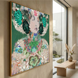 Large framed wall art featuring a colorful abstract portrait with floral and leaf motifs, hung on a beige wall in a modern interior with a glass window and wooden bench.